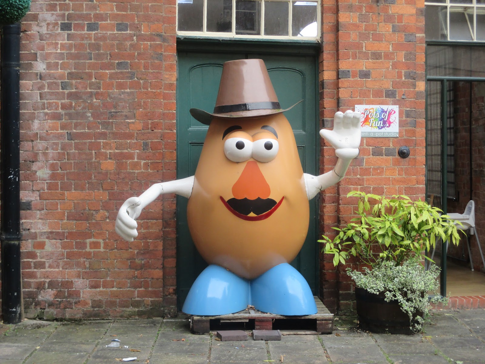 Mr Potato Head statue at De Bradelei Shopping Village in Belper, waving against a red brick wall
